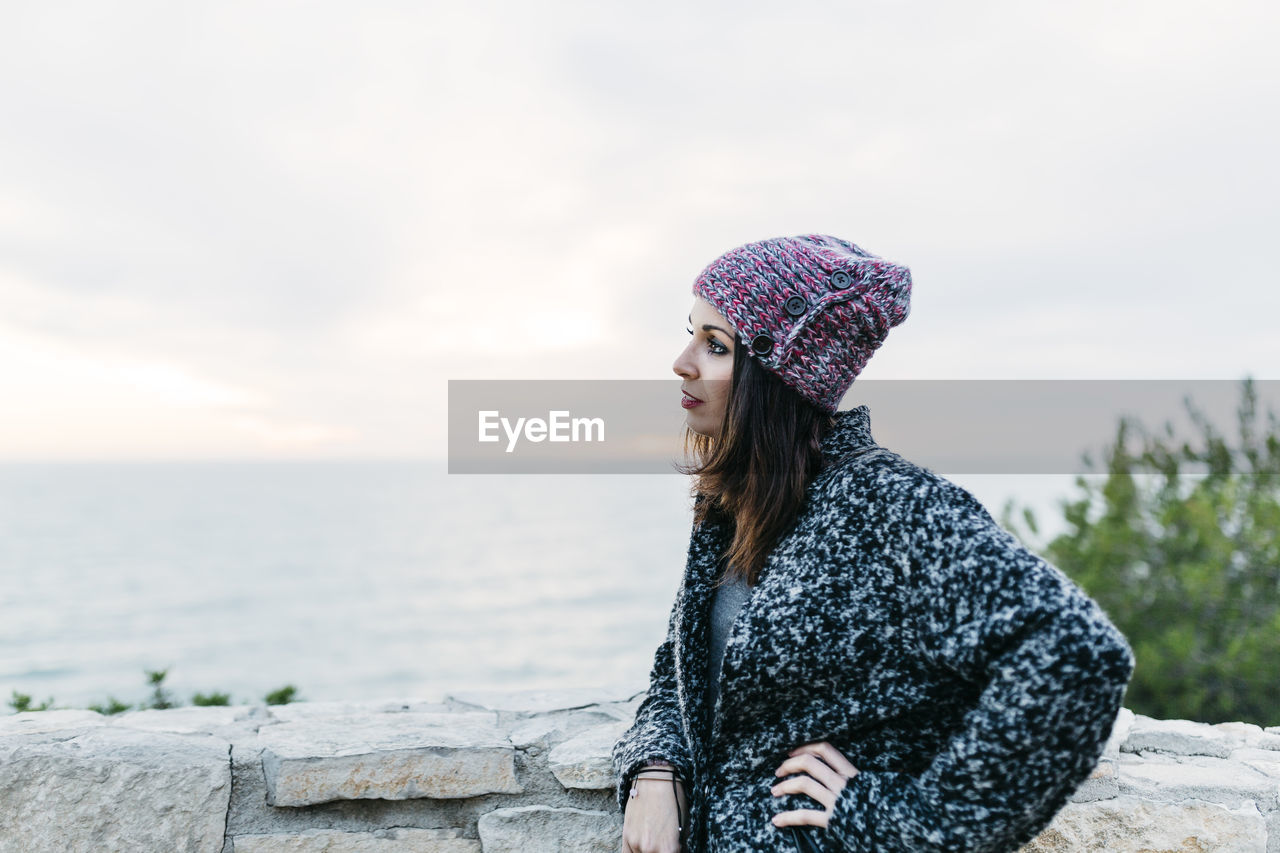 Side view of young woman standing at beach against sky