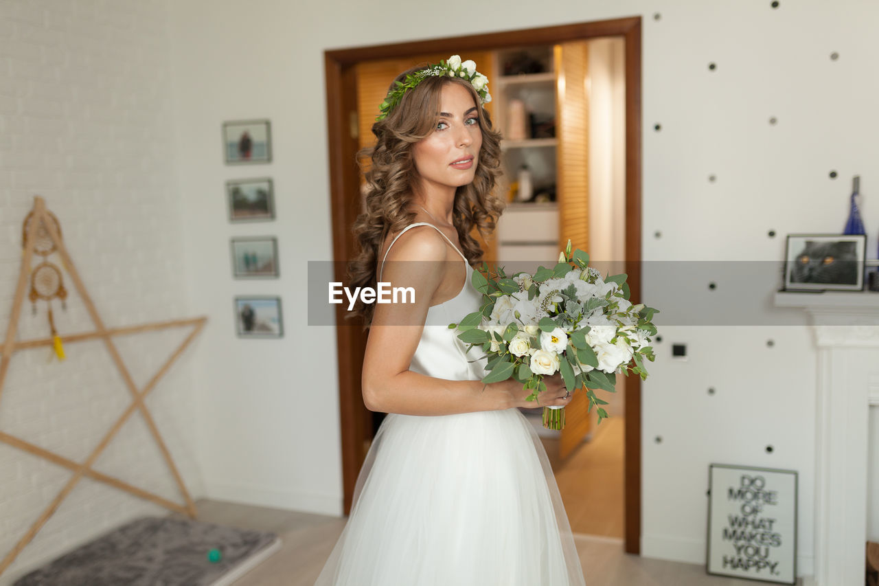 Side view portrait of young bride holding bouquet at home