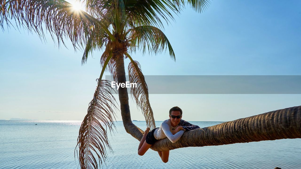 Man sitting on tree trunk at beach against sky