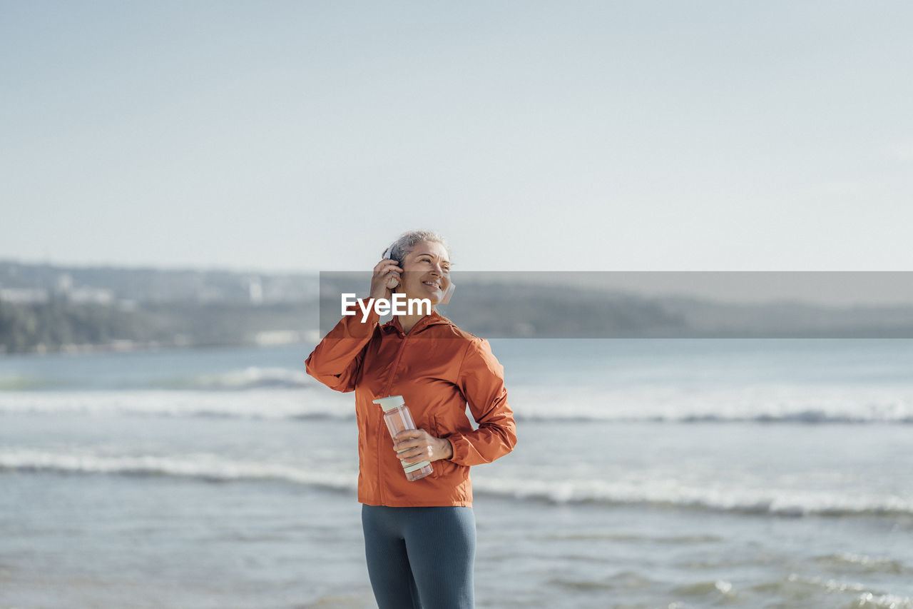 Smiling woman listening to music through headphones on beach