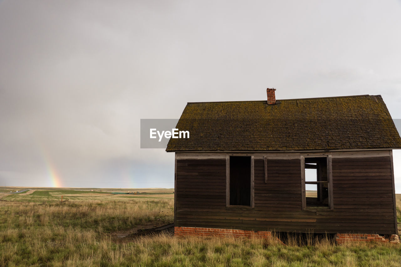 Abandoned cottage on field against cloudy sky