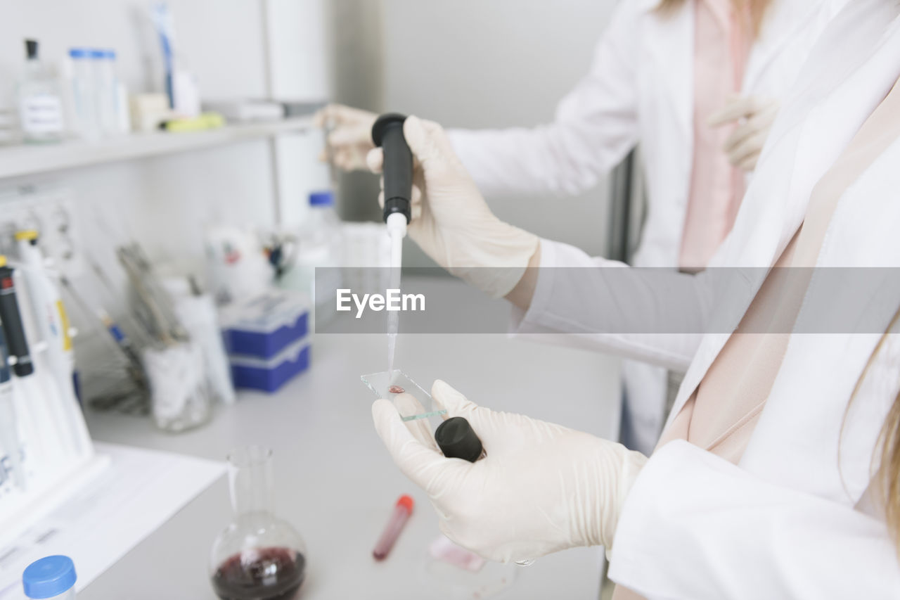 Scientists in white coats preparing sample on microscope slide in lab