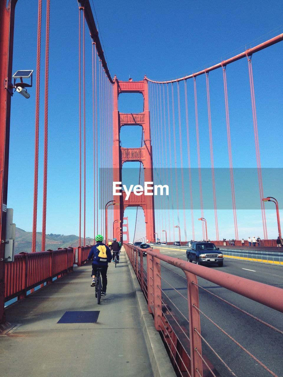 People riding bicycle on golden gate bridge against clear blue sky