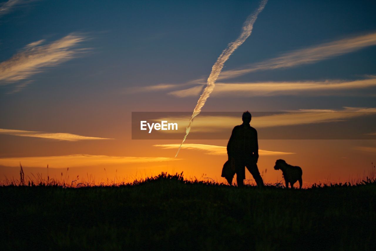 Silhouette  man and dog on field against sky during sunset
