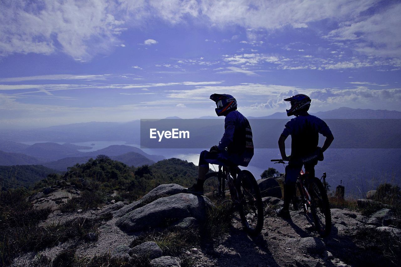 MEN RIDING BICYCLES ON MOUNTAIN AGAINST SKY