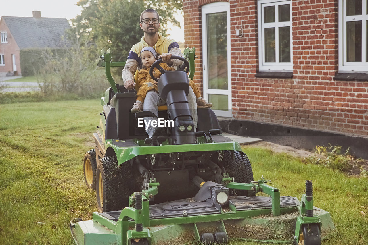 Man with a little daughter mows the lawn near the house in autumn