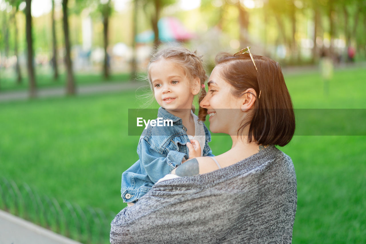 Smiling mother carrying cute daughter in park