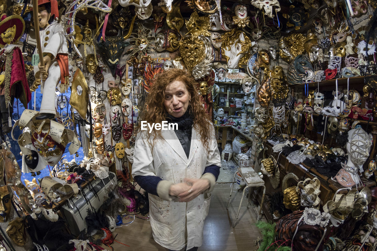 Portrait of woman smiling while standing amidst masks in store