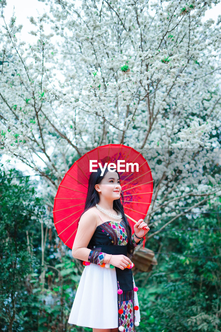 Young woman with umbrella standing against trees