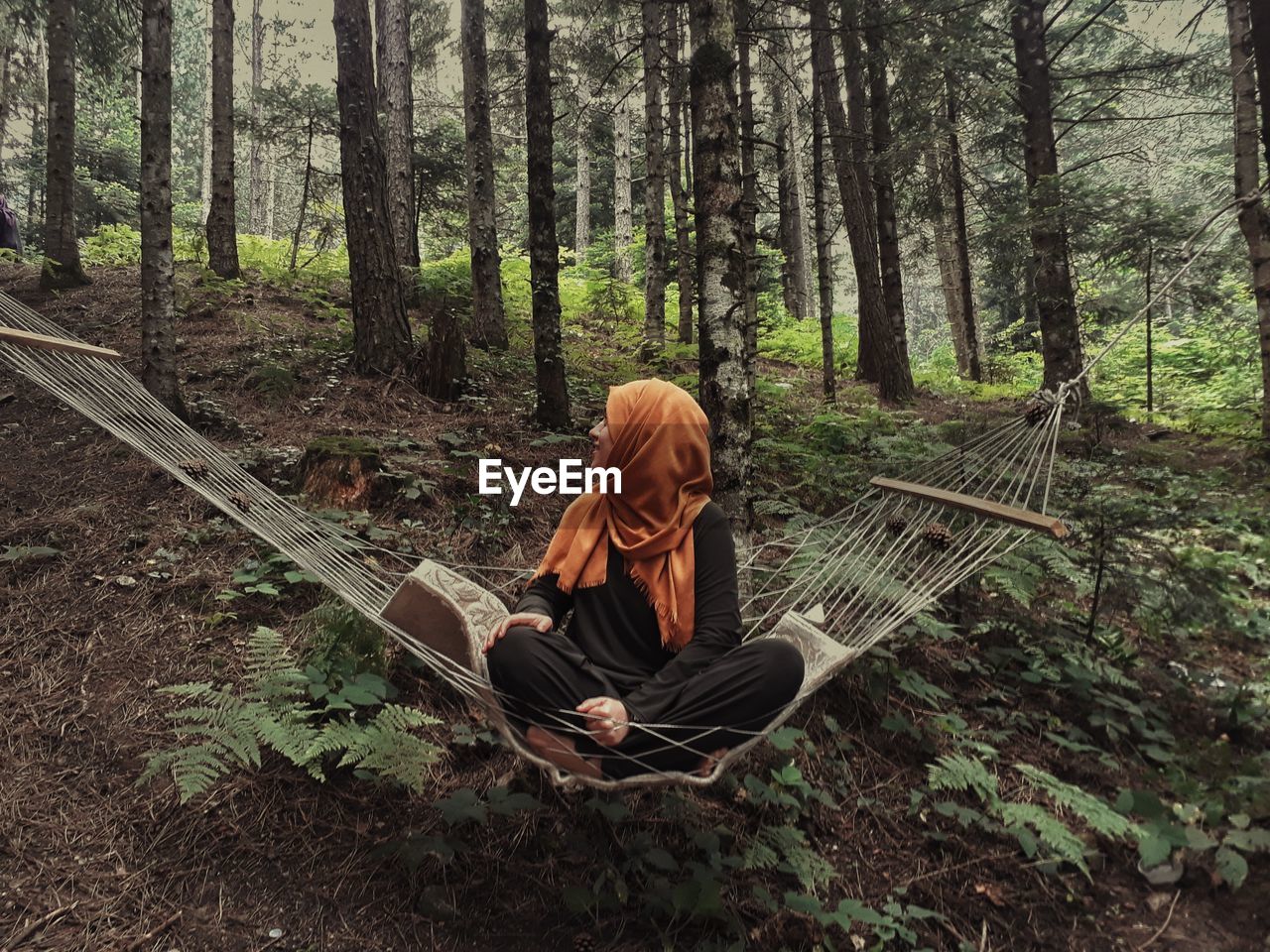 Full length of woman sitting on hammock in forest