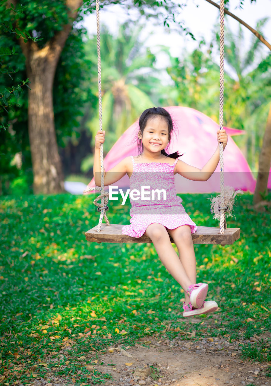 Portrait of smiling girl sitting on swing in park