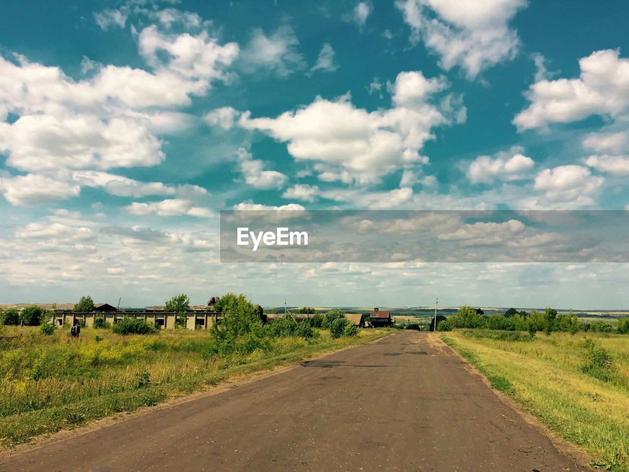 Road passing through field against cloudy sky