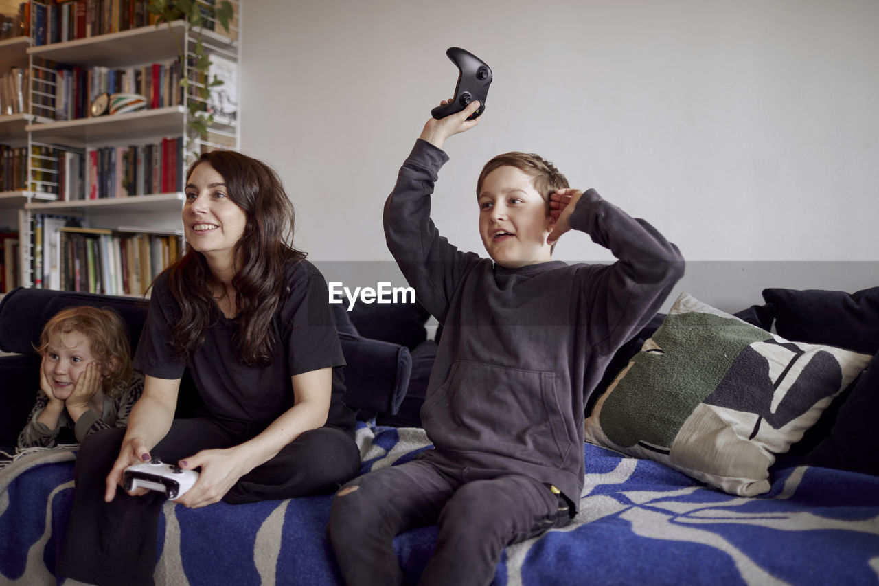 Mother with sons sitting on sofa and playing video games