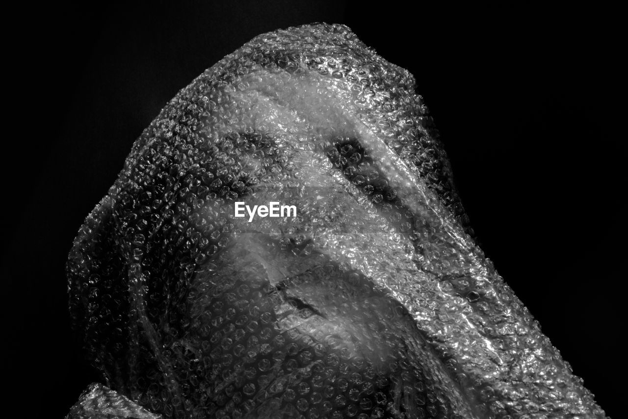 Close-up of woman in bubble wrap against black background