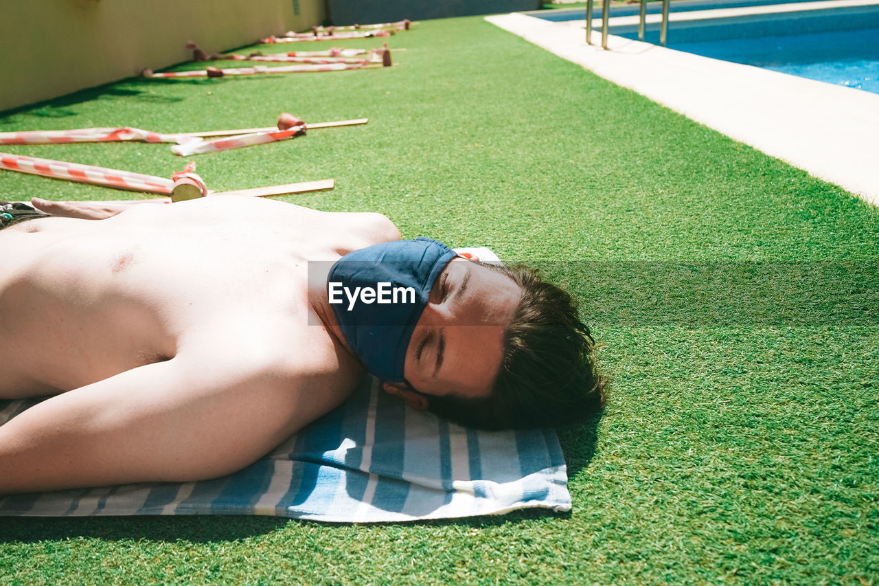 Shirtless man lying on grass by swimming pool