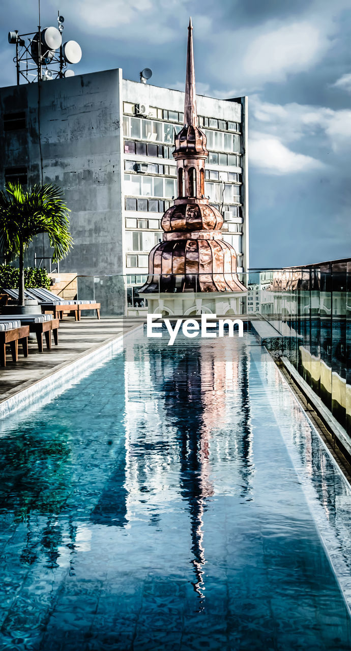 REFLECTION OF BUILDING IN SWIMMING POOL AGAINST SKY