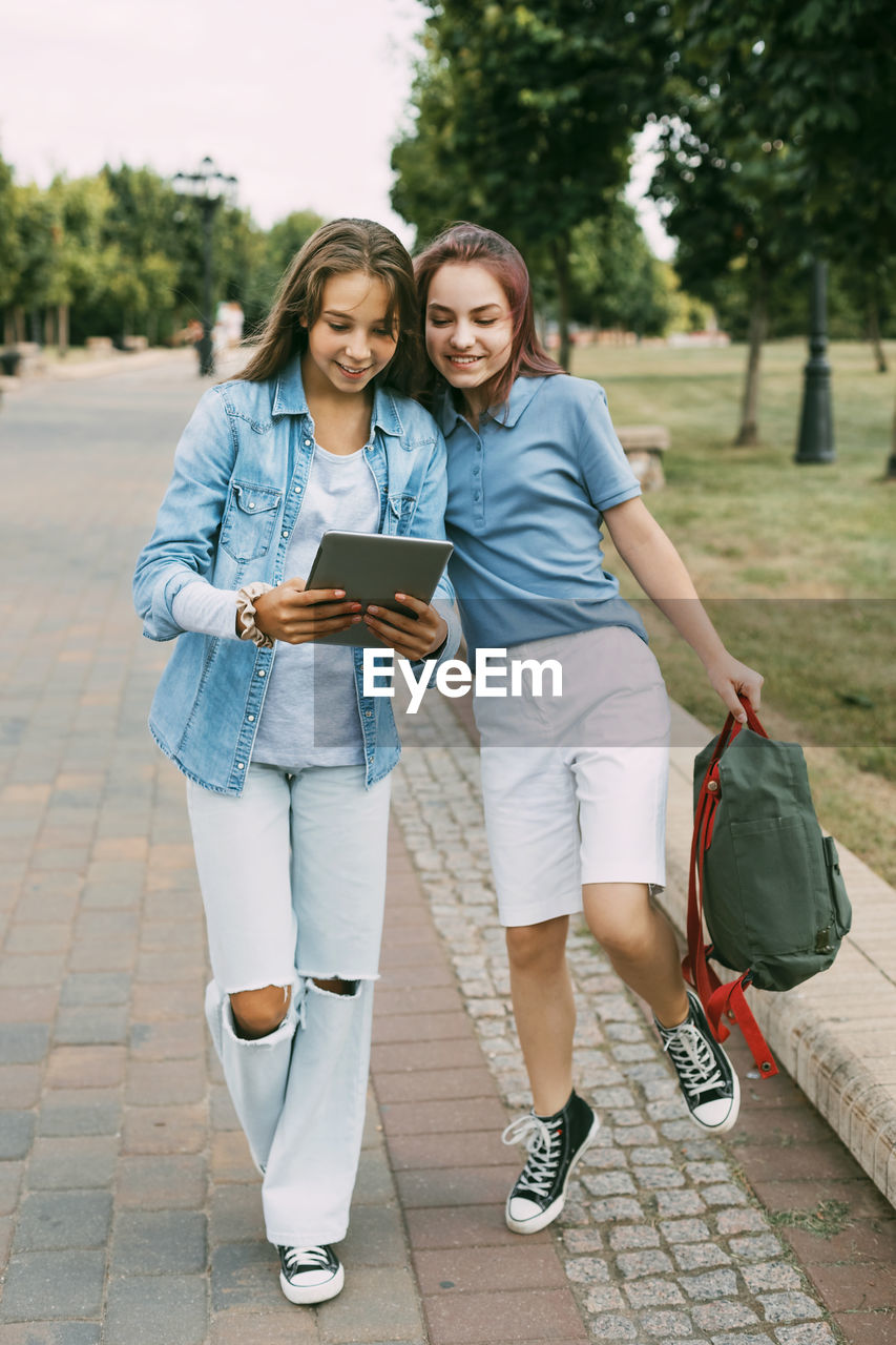 Two schoolgirls are holding a tablet in their hands and watching a video, laughing on the way 