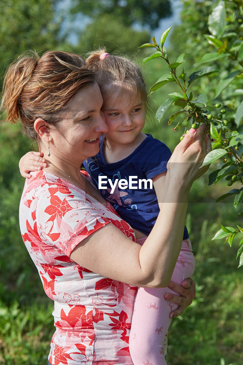 Smiling mother with daughter touching plants at agricultural field