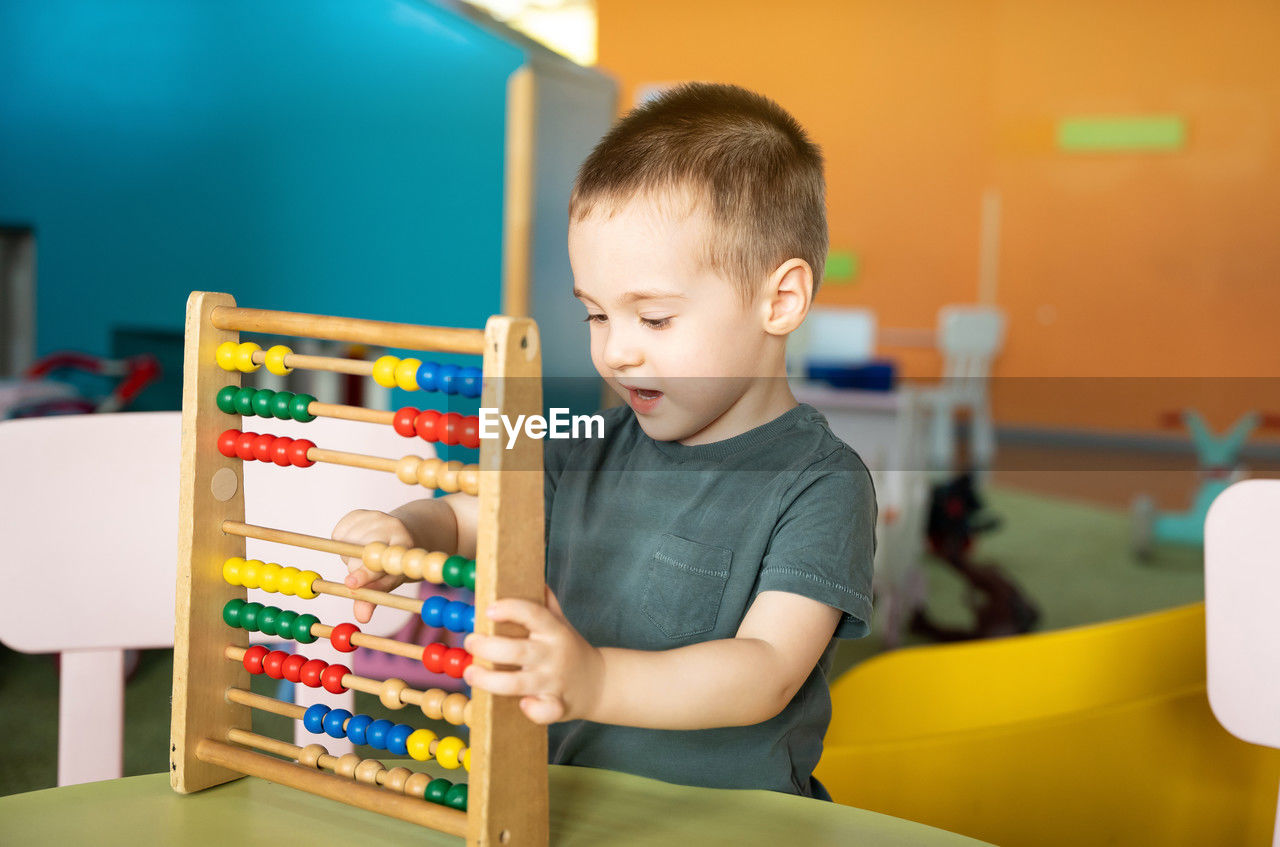 Smiling toddler boy playing with colourful toy abacus in a children's entertainment center. 