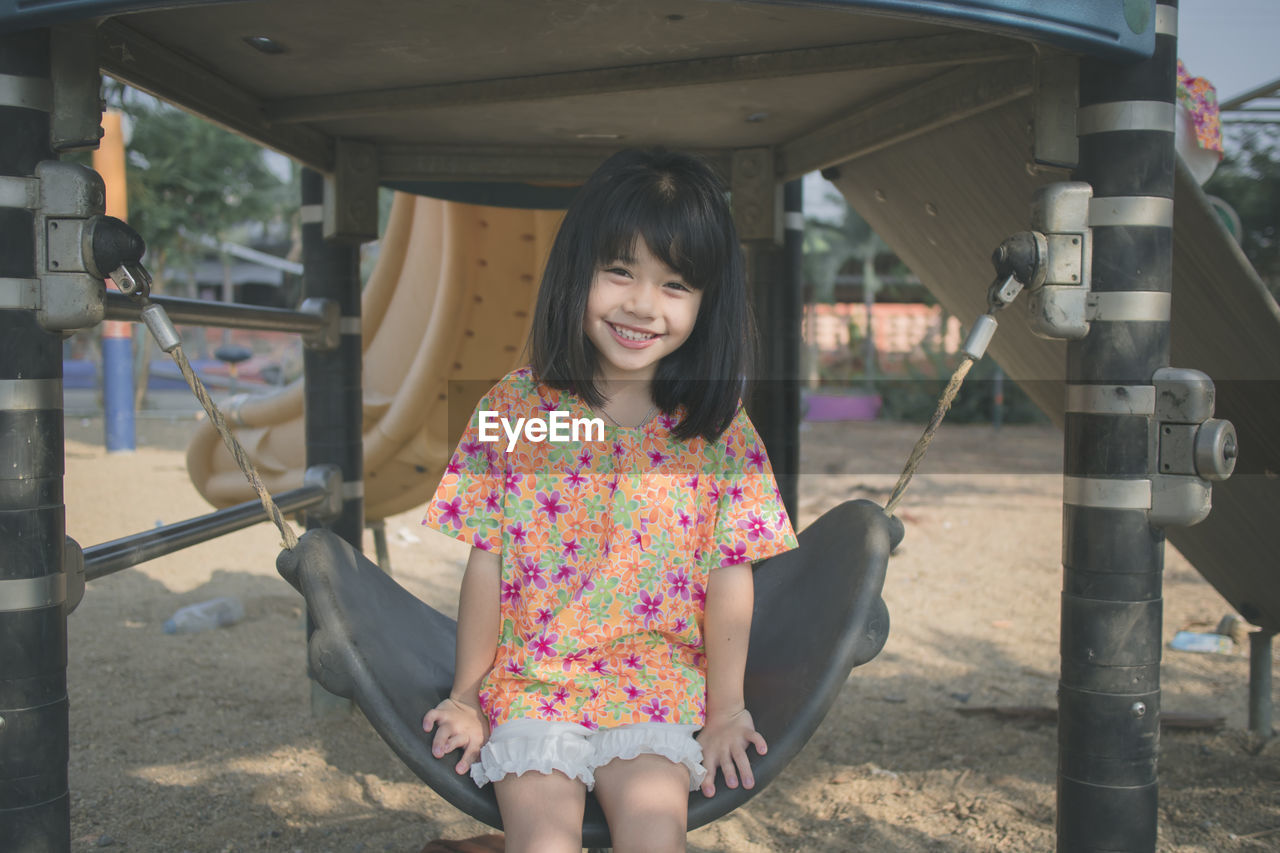 Portrait of smiling cute girl sitting on swing in park