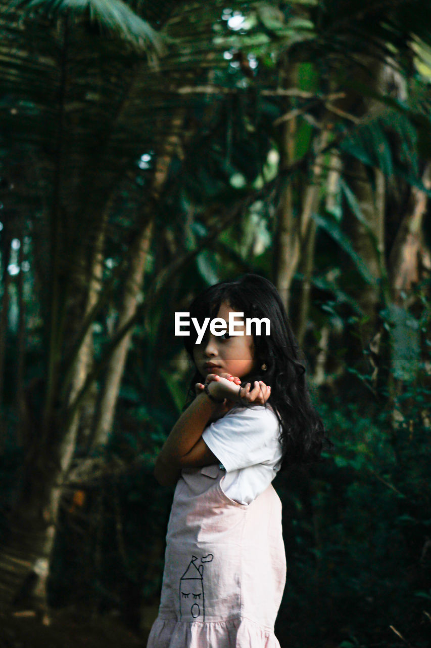 Girl looking away while standing on tree