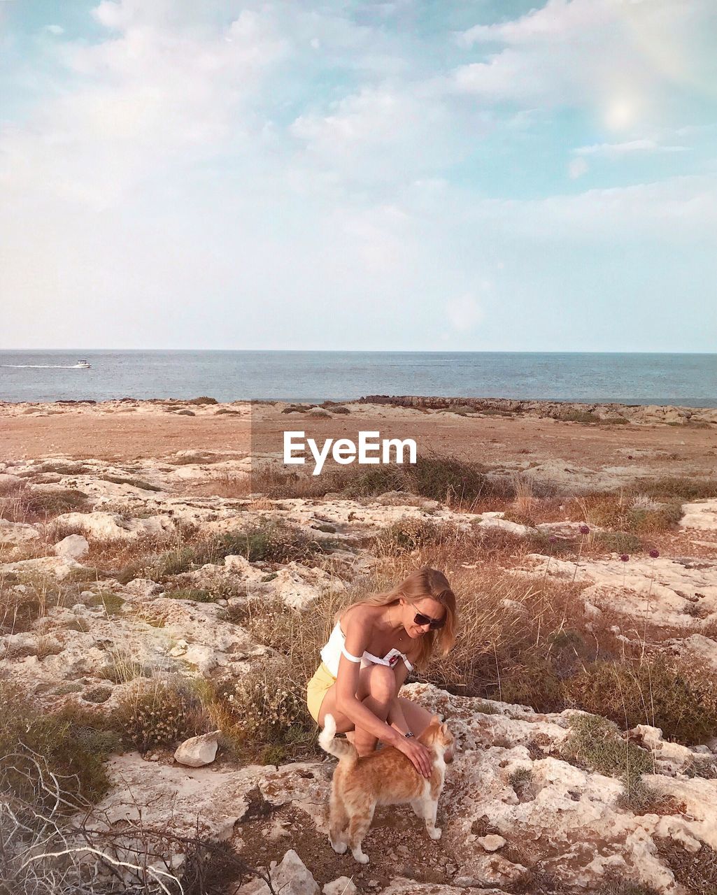 High angle view of woman with cat on rock against sea and sky