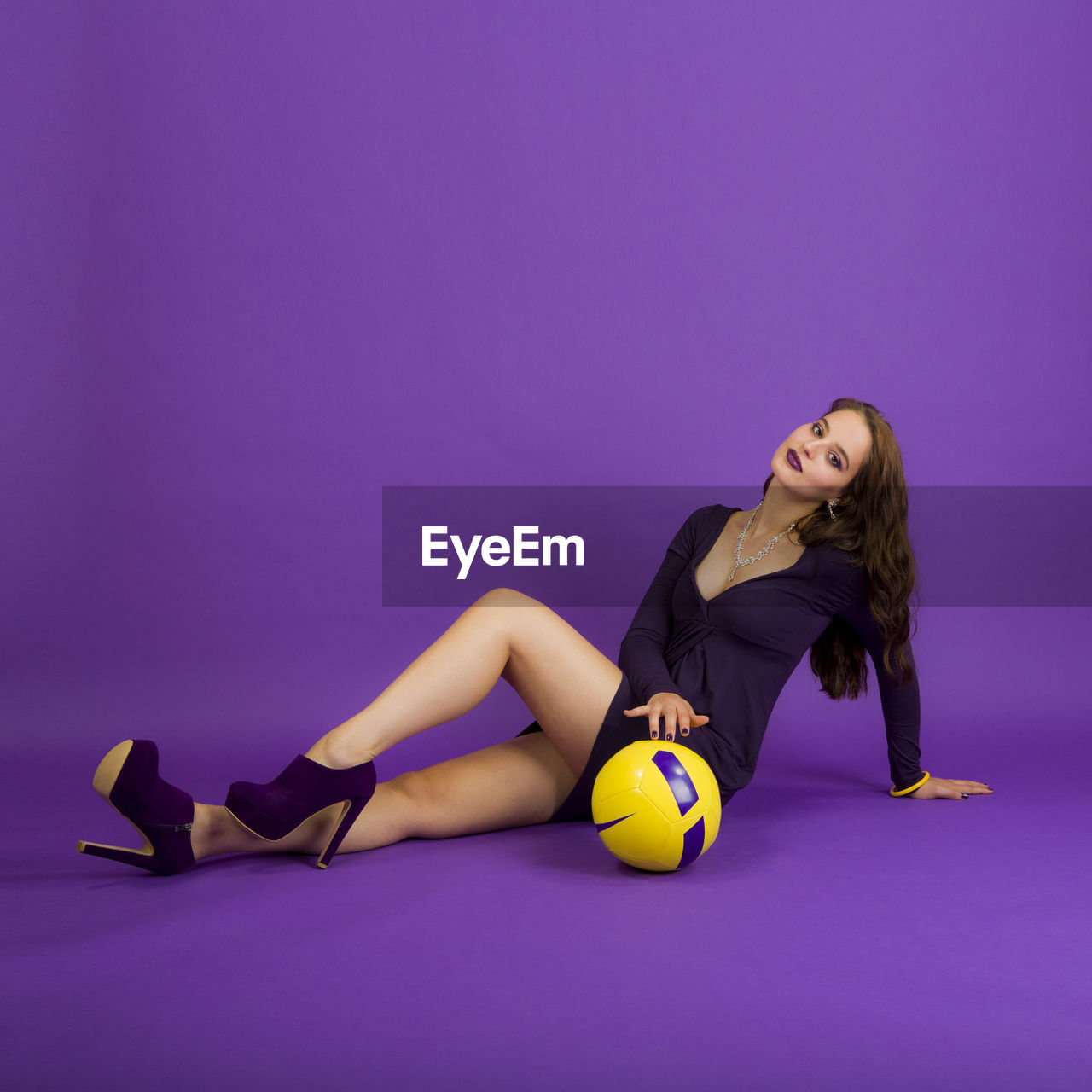 Portrait of young woman sitting with ball against purple background