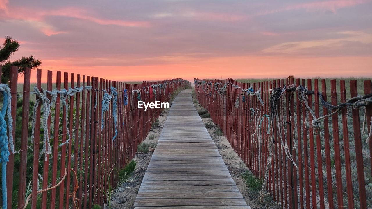 EMPTY WOODEN BOARDWALK LEADING TOWARDS ORANGE SKY