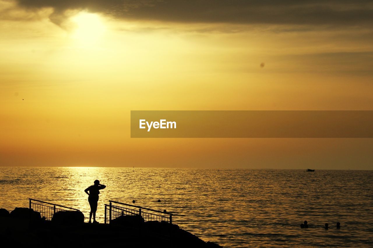 Silhouette man in sea against sunset sky