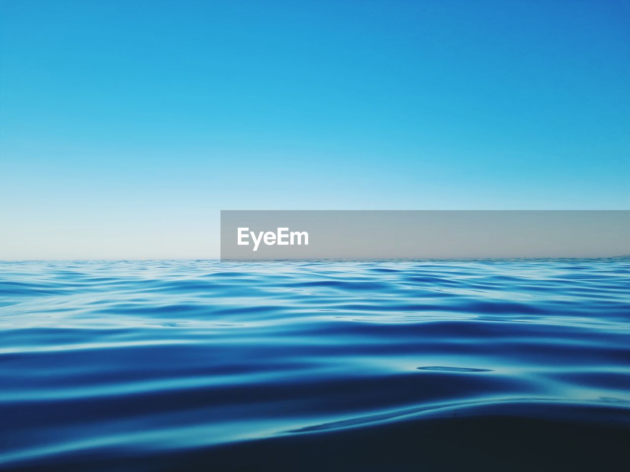 SURFACE LEVEL VIEW OF SEA AGAINST CLEAR BLUE SKY