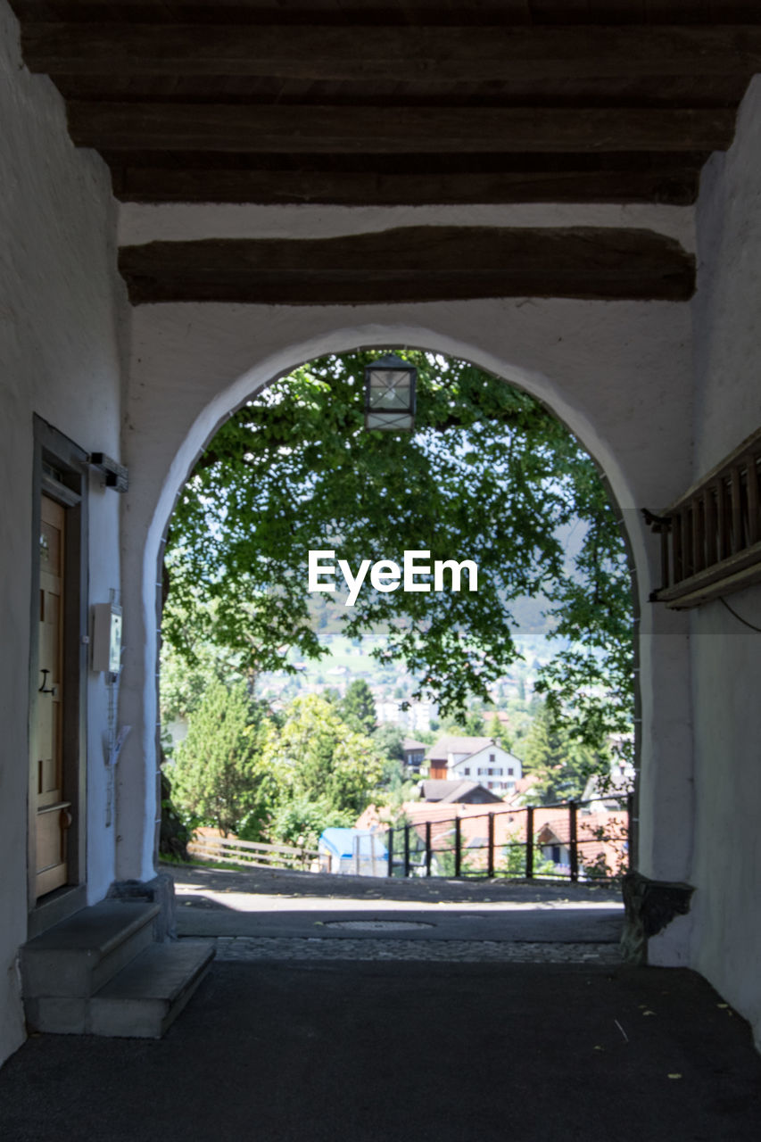 TREES AND BUILDINGS SEEN THROUGH ARCH WINDOW OF HOUSE