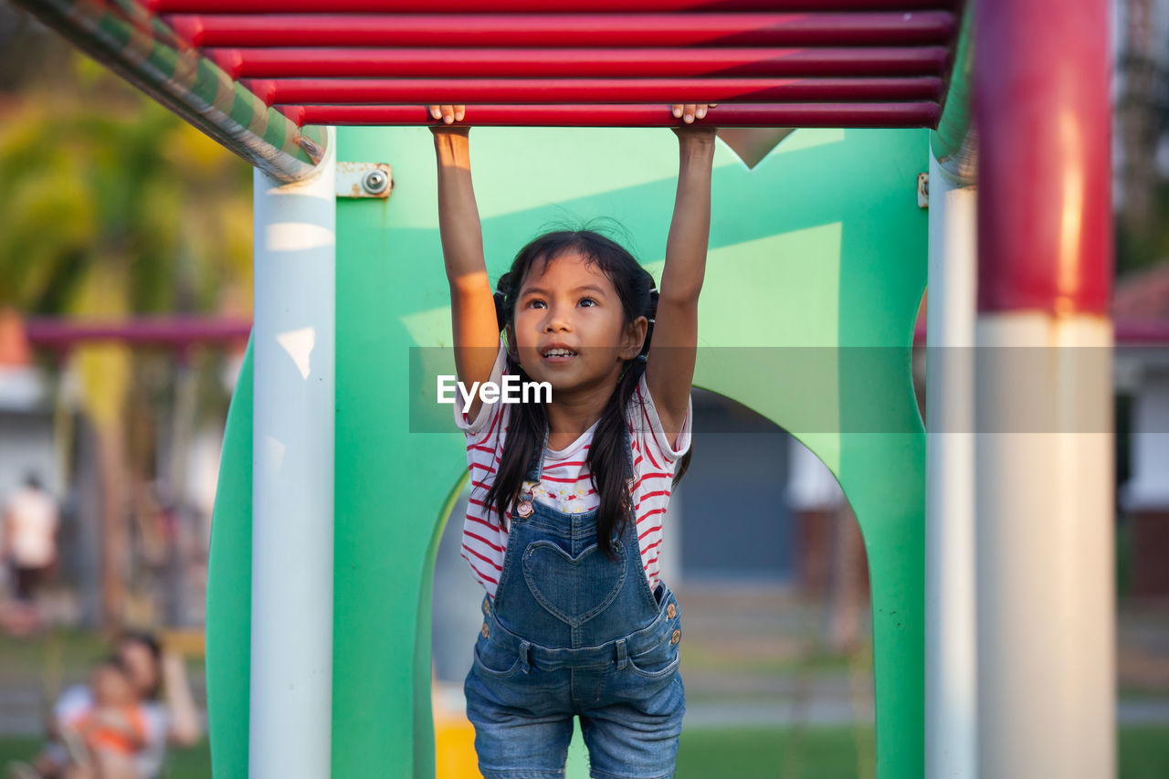 Cute girl hanging on monkey bars at playground