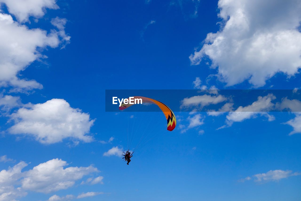 Low angle view of people on paragliding against cloudy blue sky