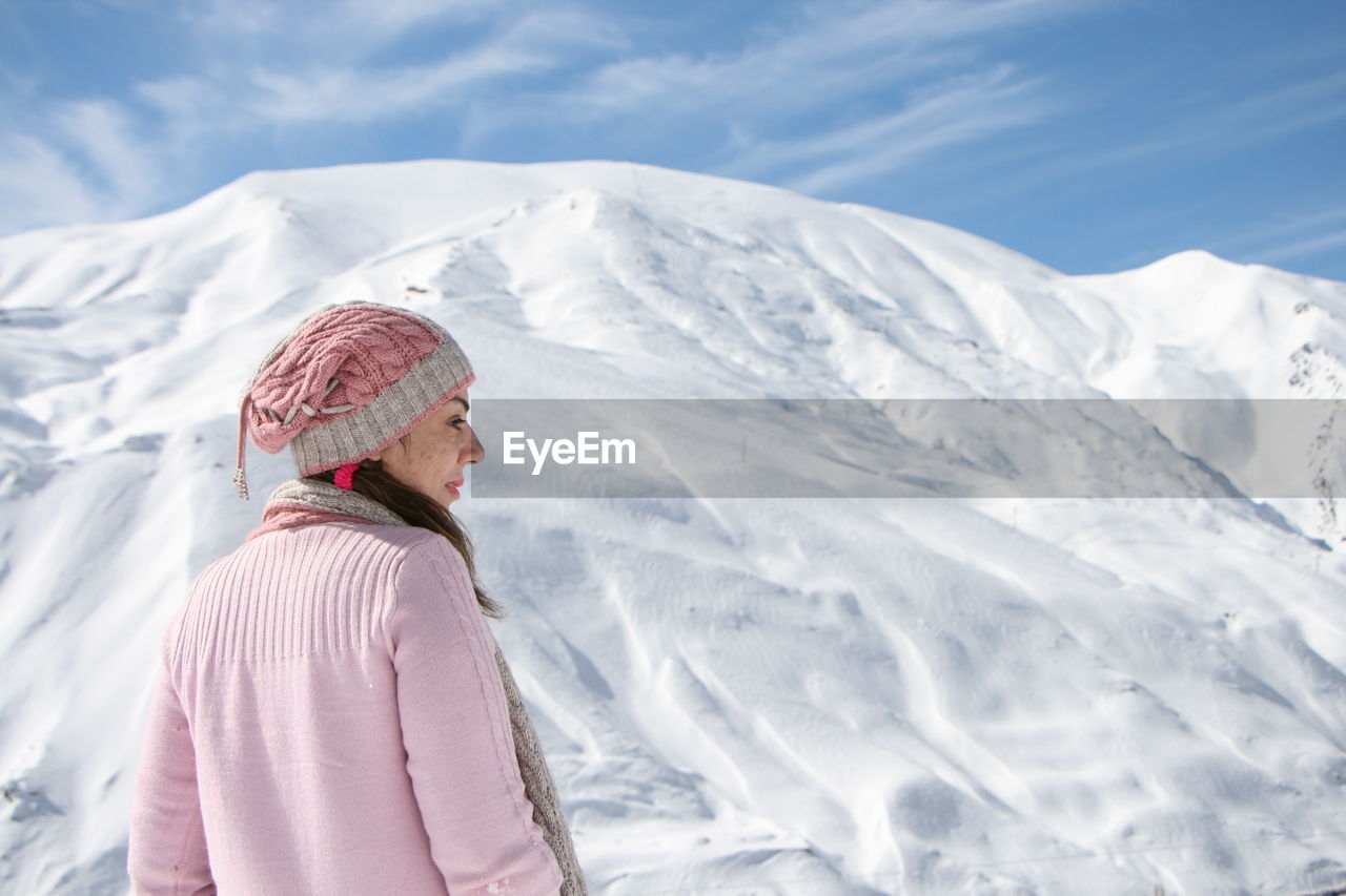 Woman in pink sweater standing against snow covered mountain against sky