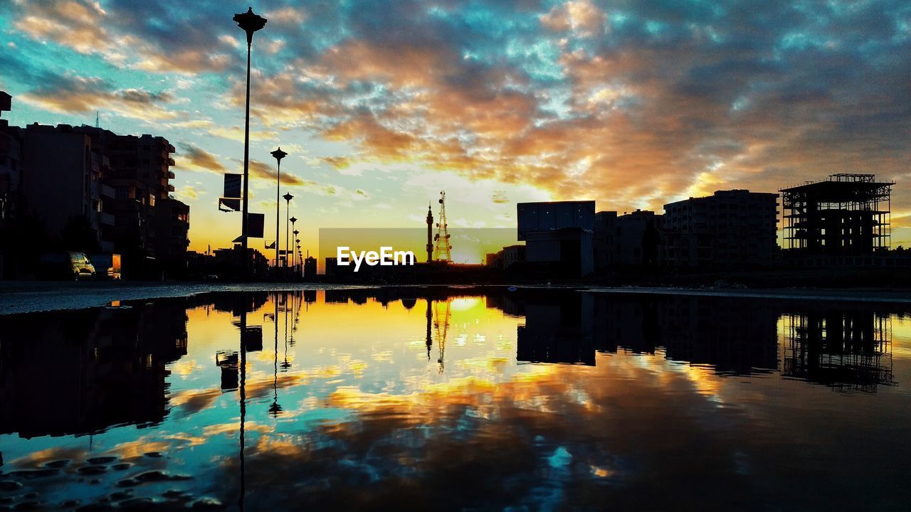 Silhouette buildings by lake against sky during sunset