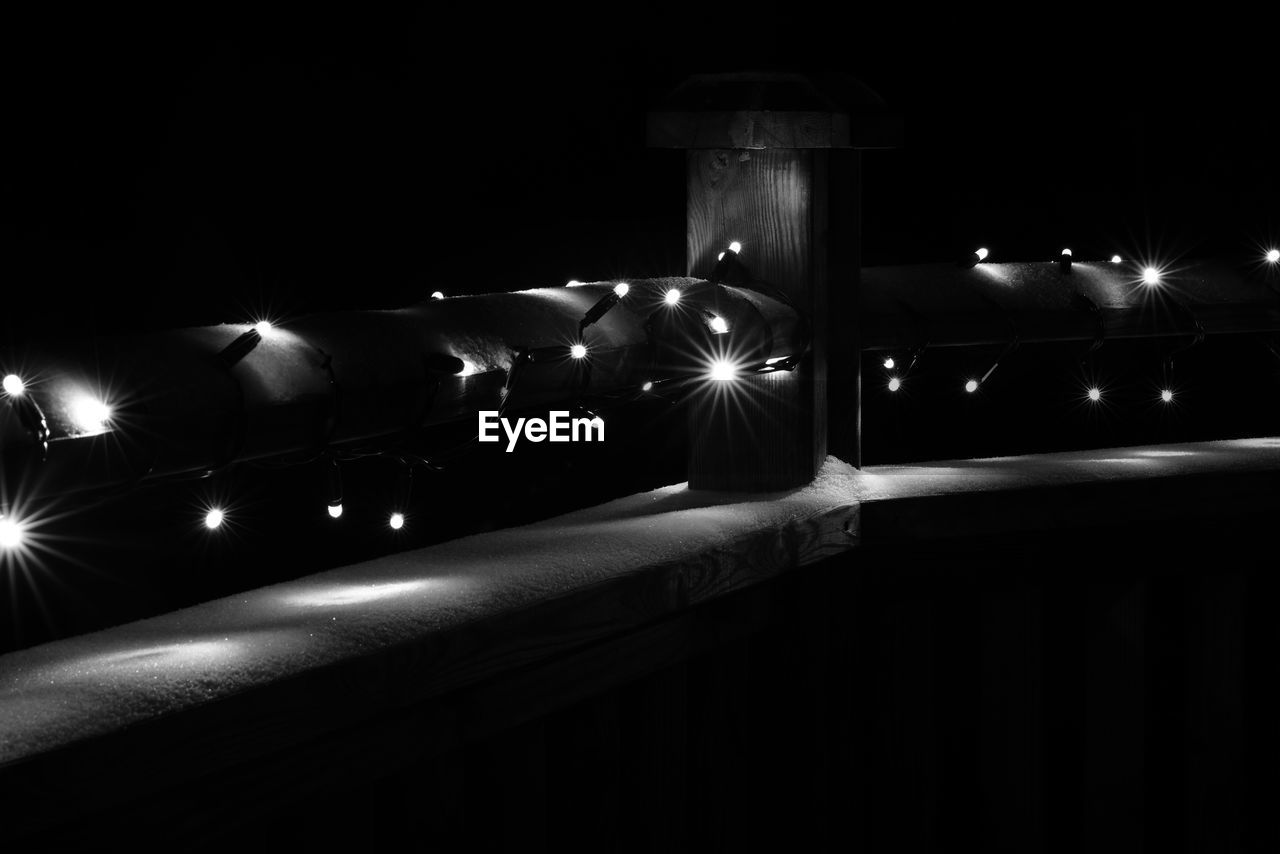 Illuminated christmas lights on railing with snow at night