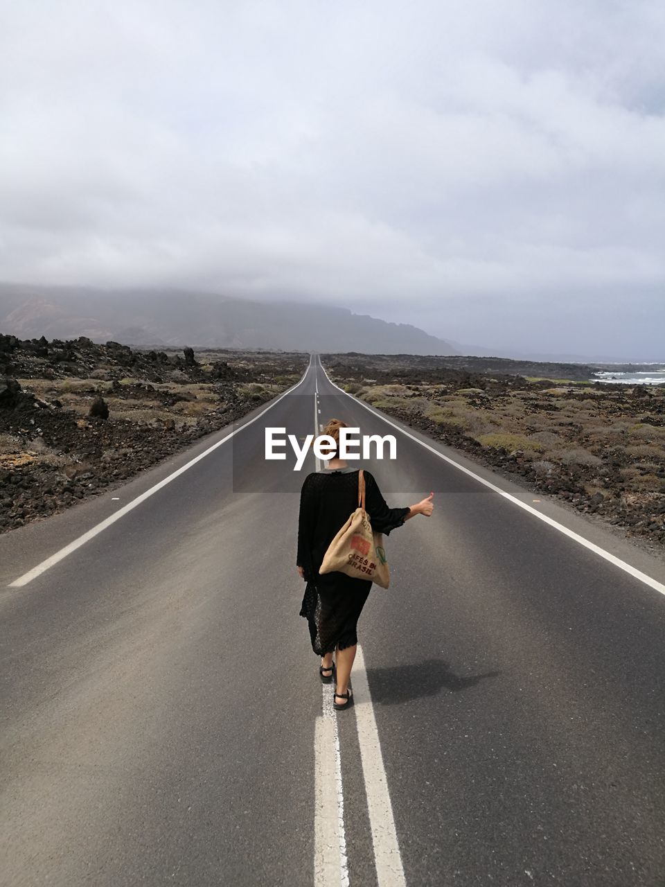 Rear view of woman hitchhiking on road against sky