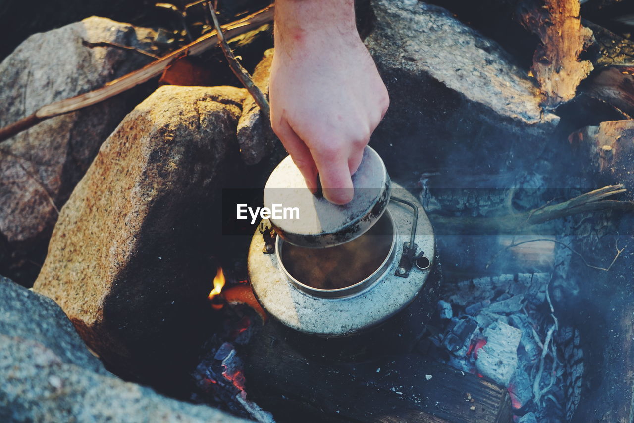 Cropped hand holding lid of container on campfire