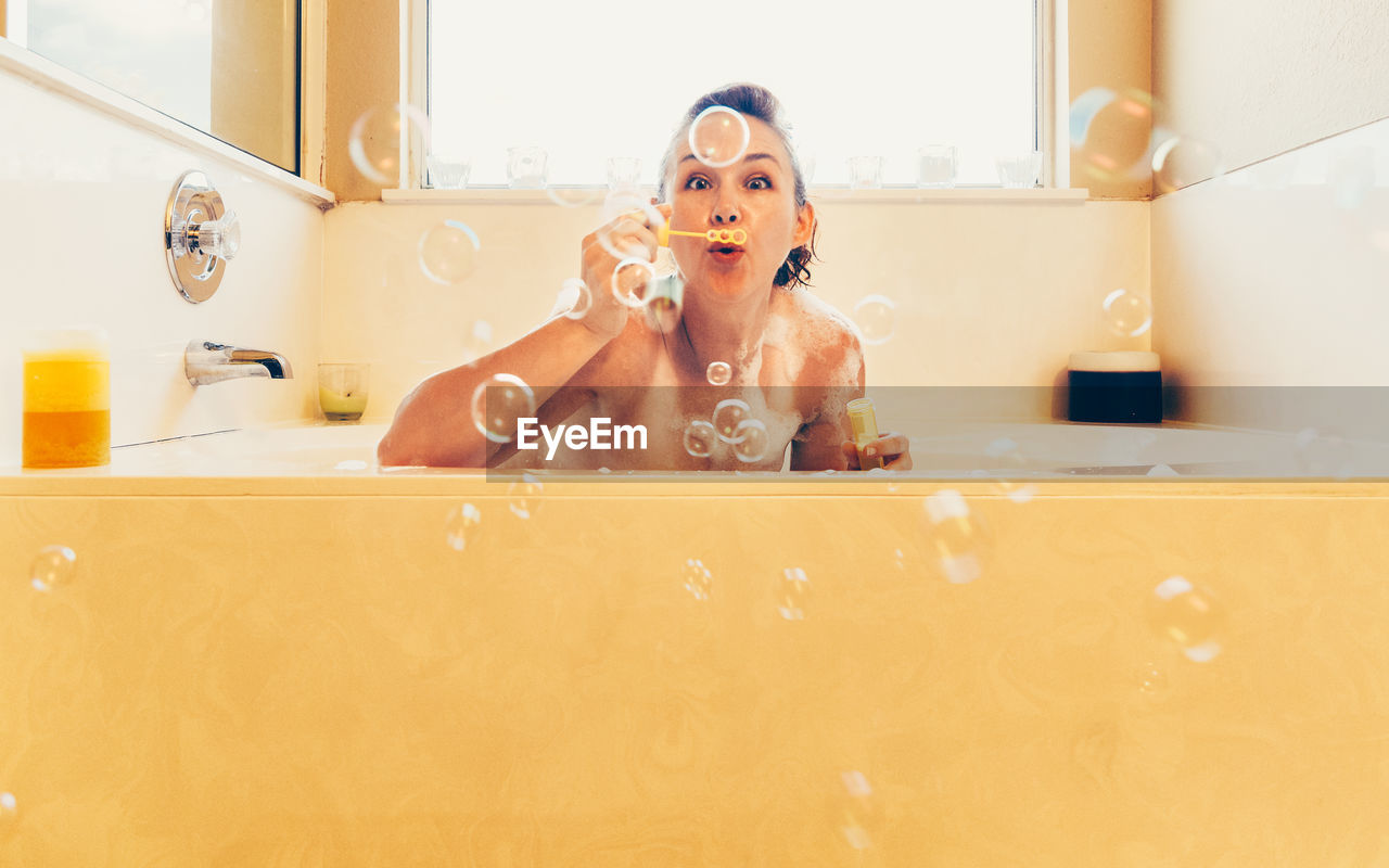 Portrait of woman blowing bubbles in bathroom