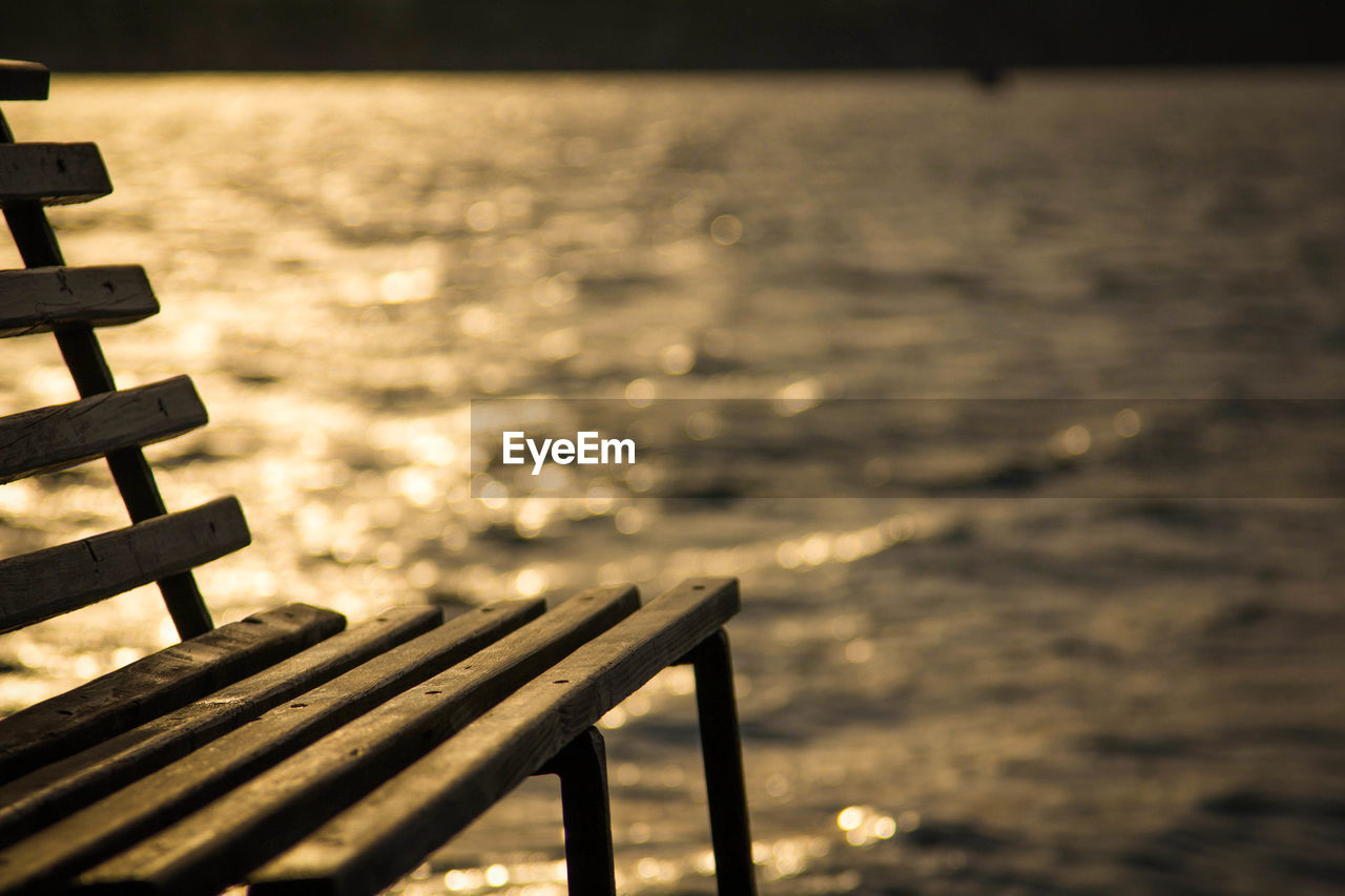 EMPTY BENCH ON BEACH AGAINST SKY