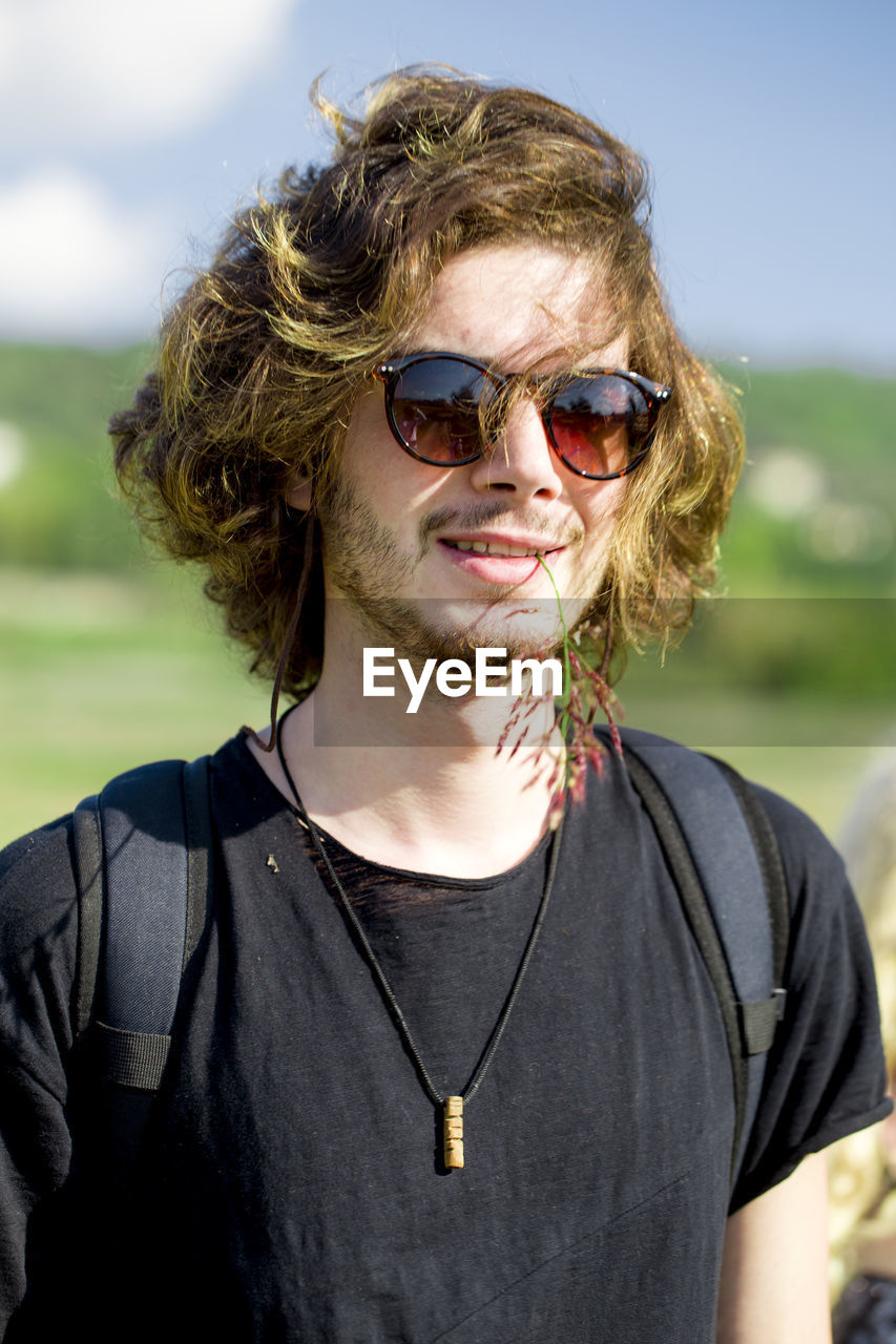 Portrait of young man wearing sunglasses while standing at farm against sky