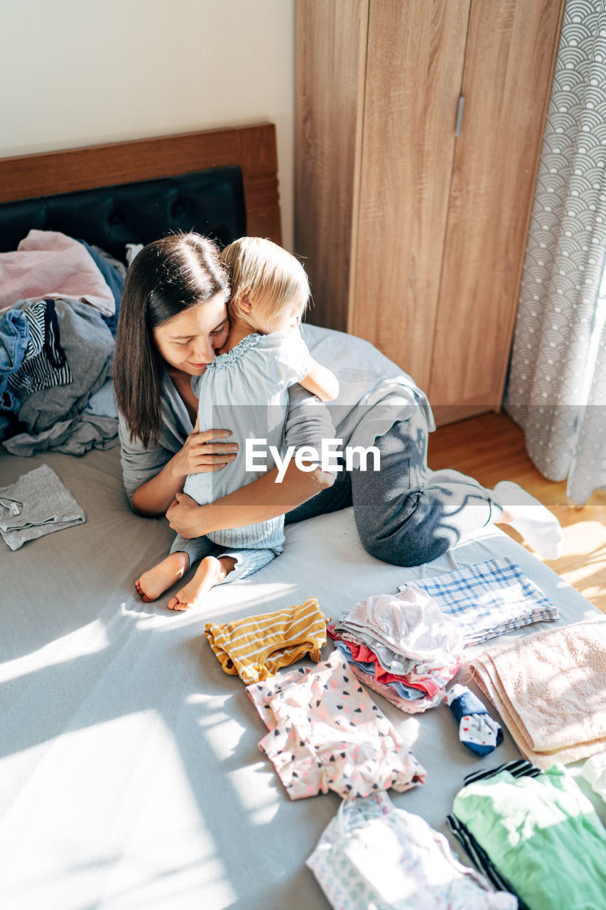 Mother embracing toddler girl in bedroom at home