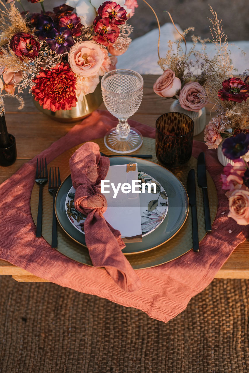 From above of wooden table setting with cutlery on plates served on cloth near colorful bouquets of flowers with wineglasses during wedding celebration