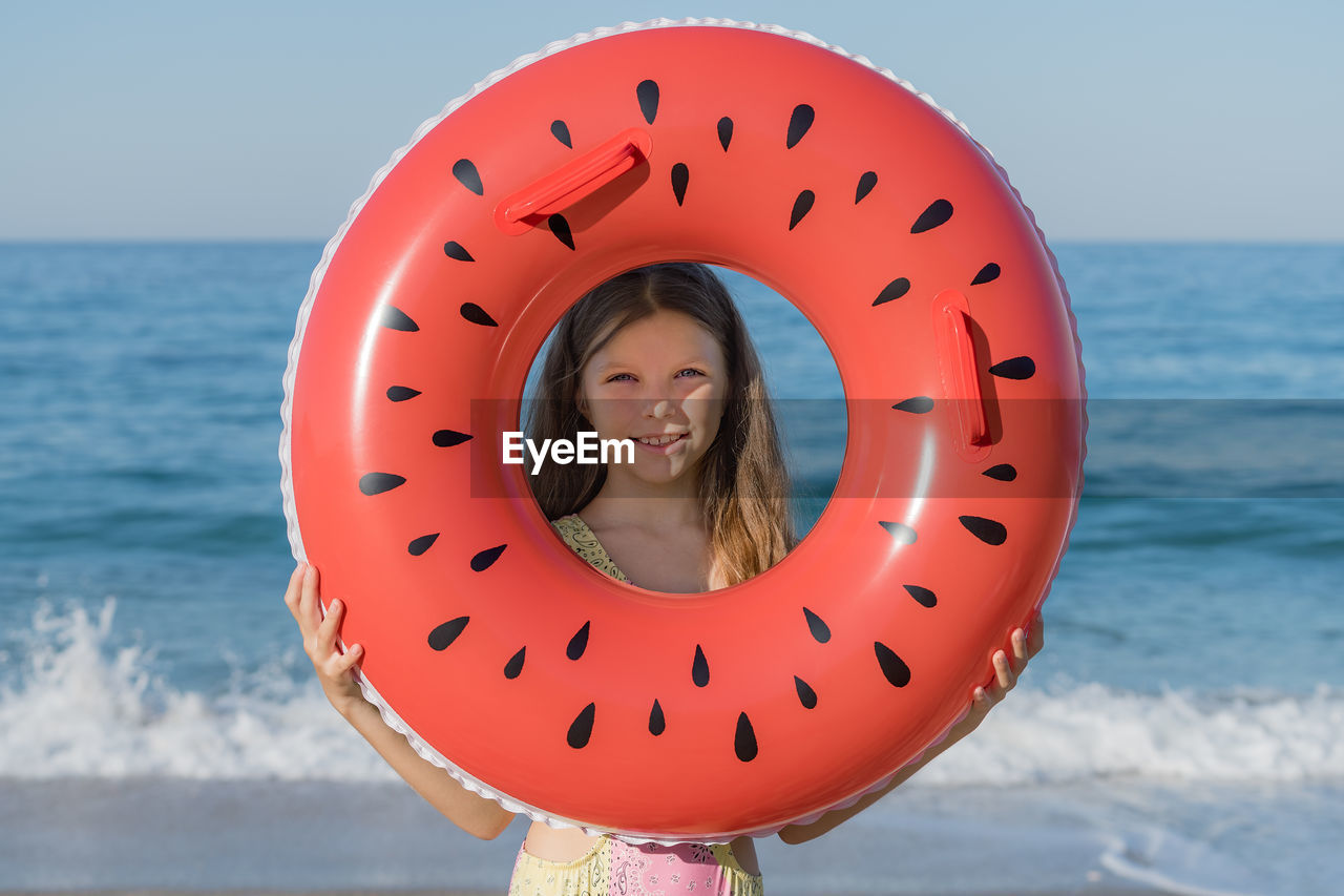 A young girl looks through an inflatable ring on the beach. summer holidays on the sea coast.