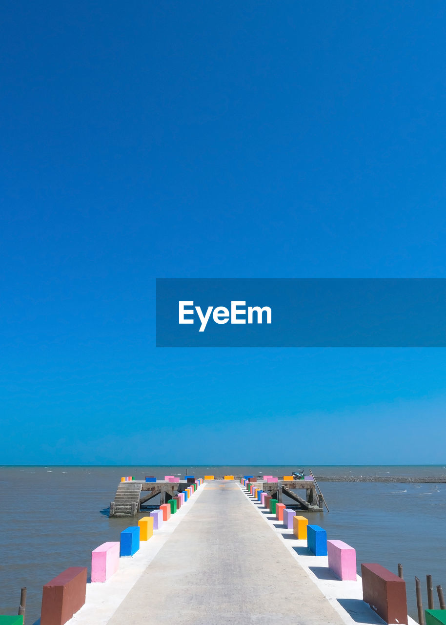 The cement bridge extends into the sea. with colorful barrier panels in the blue sky