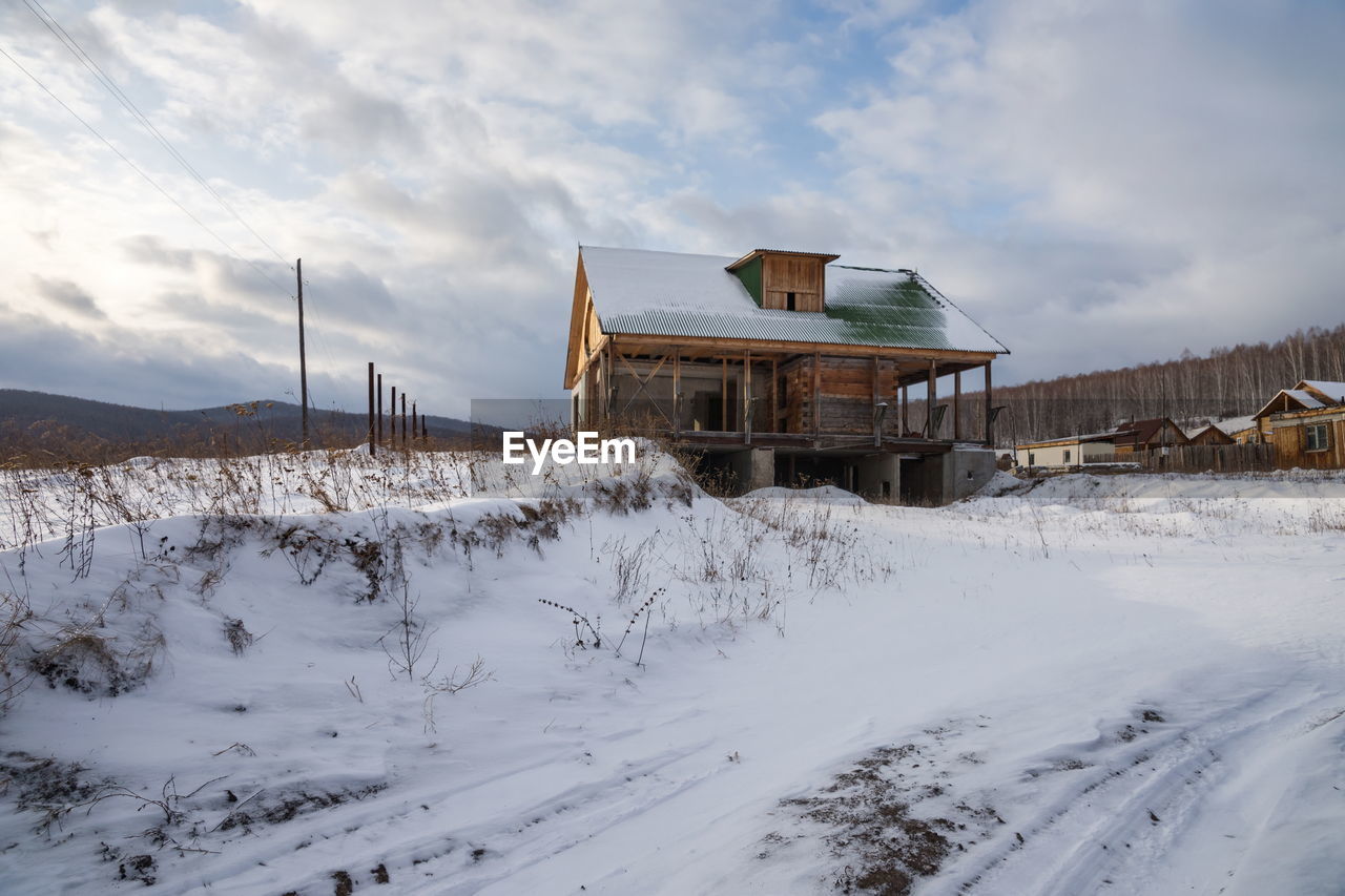 A dacha under construction stands on a hillock on the outskirts of the village in winter.