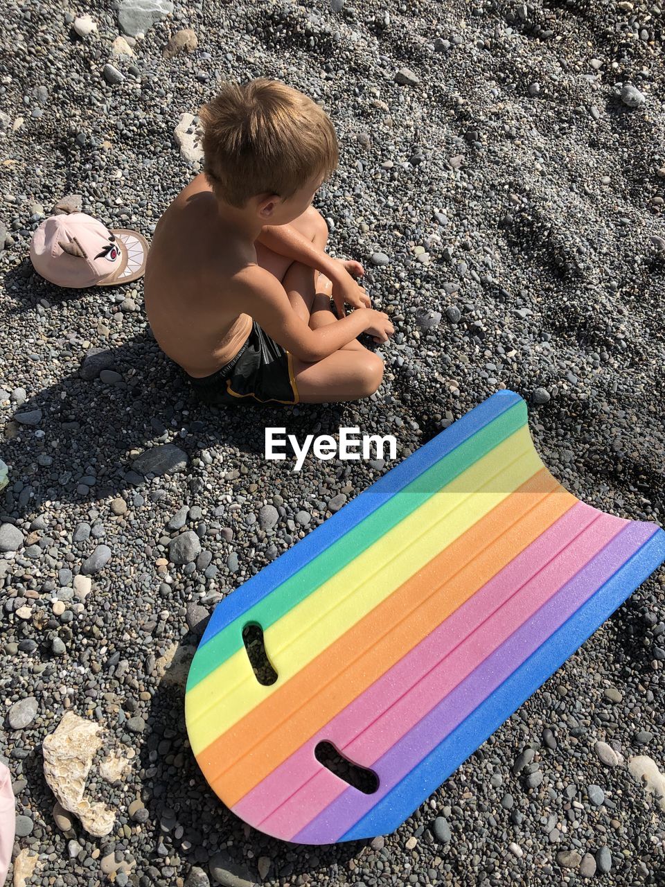 High angle view of boy sitting by body board at beach