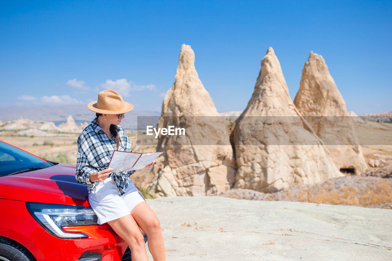 rear view of woman sitting on rock formations against sky