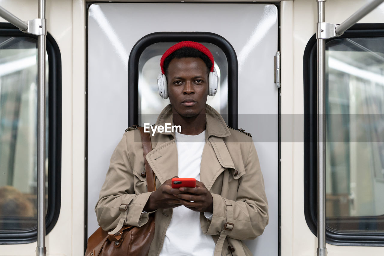 Black man in subway train using smartphone listens to music with headphones in public transportation