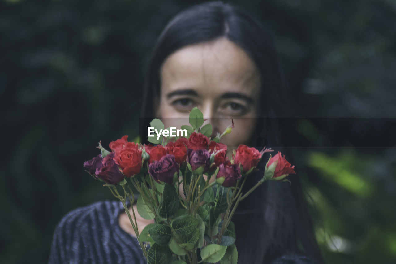 Beautiful woman posing in her garden., holding flowers up to the camera.